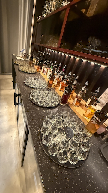 Mehrere Degustationsgläser auf Tabletts und diverse Macardo Flaschen auf einem Tresen. Die leeren, klaren Gläser sind bereit für eine Verkostung. Im Hintergrund erhellt eine Fensterfront den Raum. Einladende Atmosphäre.